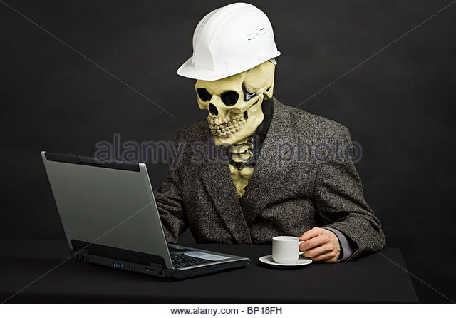 A skeleton wearing a construction hat sitting at a desk looking at a computer.